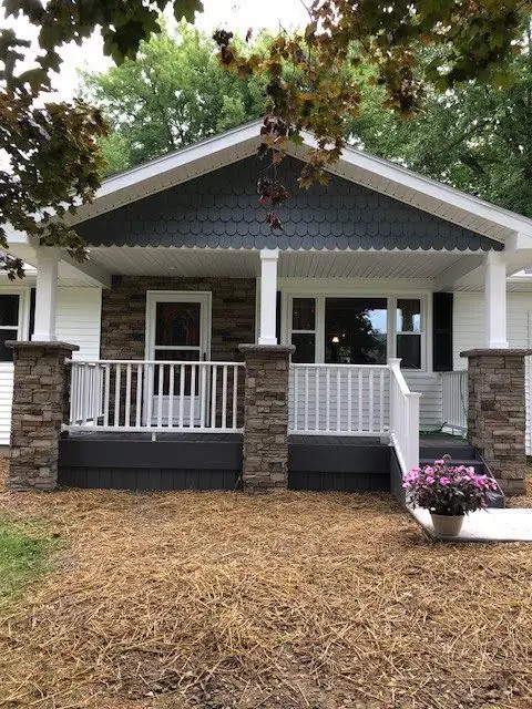 Covered front porch with stone veneer column bases, white railings and a gray shingle gable